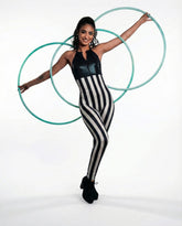 Woman poses with three hula hoops wearing a black and white striped spandex catsuit with a front zipper, a hologram halter top jumpsuit, and full body stretch performance wear against a white background.
