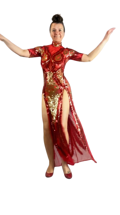 A woman in a Red And Gold Sequin Sheer Dress, sleeveless with hand accessories, stands confidently with arms raised against a white background.