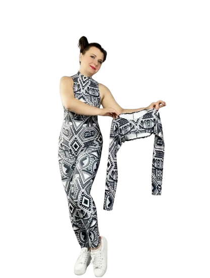 A woman wears the Geometric Catsuit with halter neck and UV-reactive tribal print, holding a matching long-sleeved crop top. The vibrant patterns create a striking glow under blacklight against a white background.