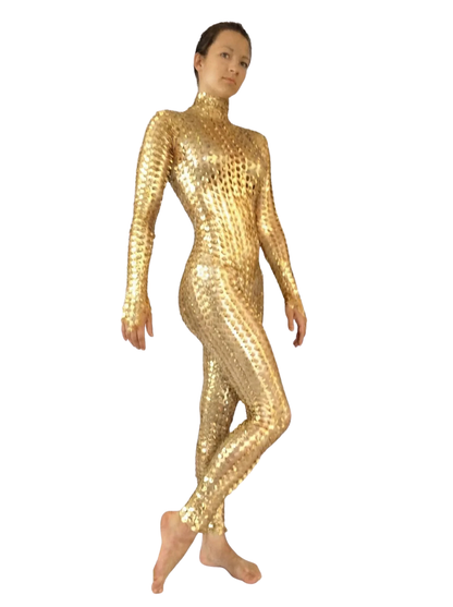 A person stands barefoot in a Metallic Gold Spiky Catsuit—a shiny, form-fitting, full-body spandex jumpsuit with a 3D texture and high neck—creating a sleek futuristic performance look.