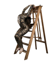 A contortionist in a Black Swirl On Holographic Catsuit with a scoop neck and full sleeves bends backward over a wooden ladder.