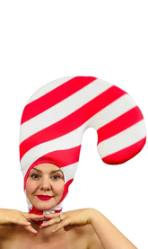 A woman smiles with hands under her chin, wearing the Candy Cane Headpiece—an open face, red and white stripe spandex hat that&