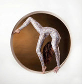 A woman wearing a White and Gold Catsuit Bodysuit with full sleeves and a round neck does a handstand inside a circular frame against a brown background.
