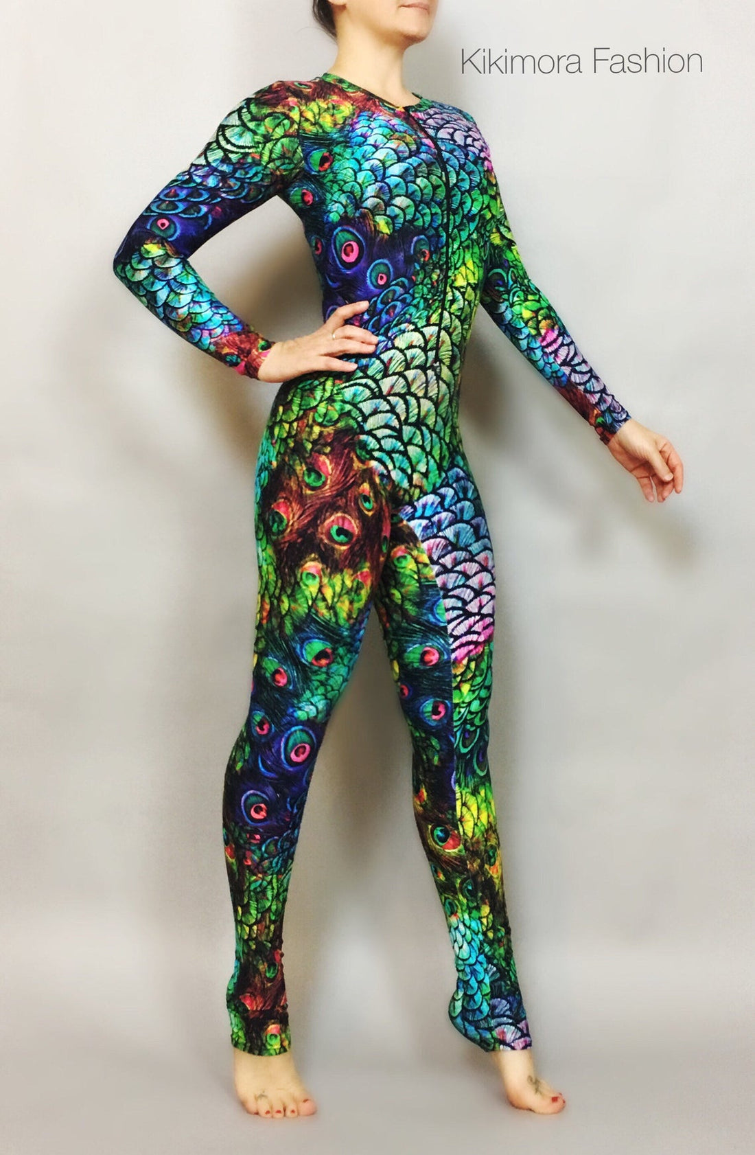 Description: Person wearing a vibrant Peacock Print Spandex Catsuit, ideal for contortionists, aerialists, or exotic dancers, standing against a plain background. Text: &quot;Kikimora Fashion - Limited Edition.