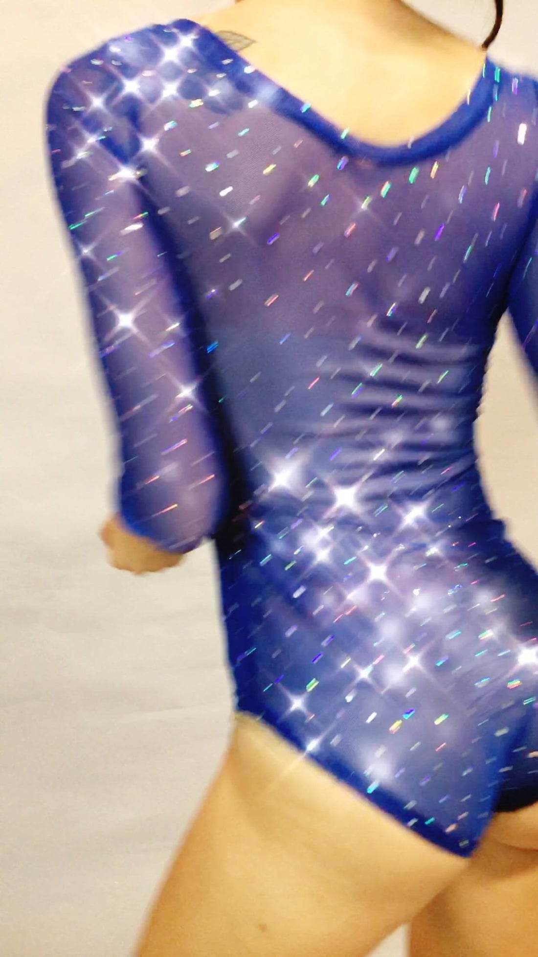 Someone is wearing a sparkly blue sheer bodysuit featuring rhinestone print polkadots on the long sleeves, set against a plain background.