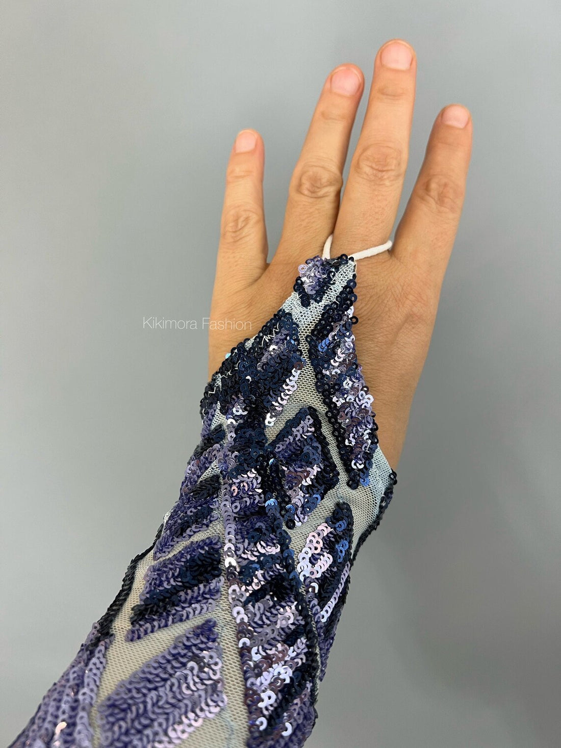 A hand adorned with a ring and a stylish sequined glove featuring a futuristic geometric blue and silver pattern on a light grey backdrop, evocative of the Beautiful Sequin Jumpsuit from the Exotic Dance Wear collection.