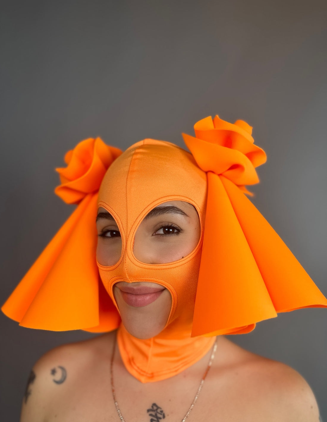 Person wearing a vibrant Circus Headpiece in an orange glow-in-the-dark design with floral details, paired with a matching mask, smiling.