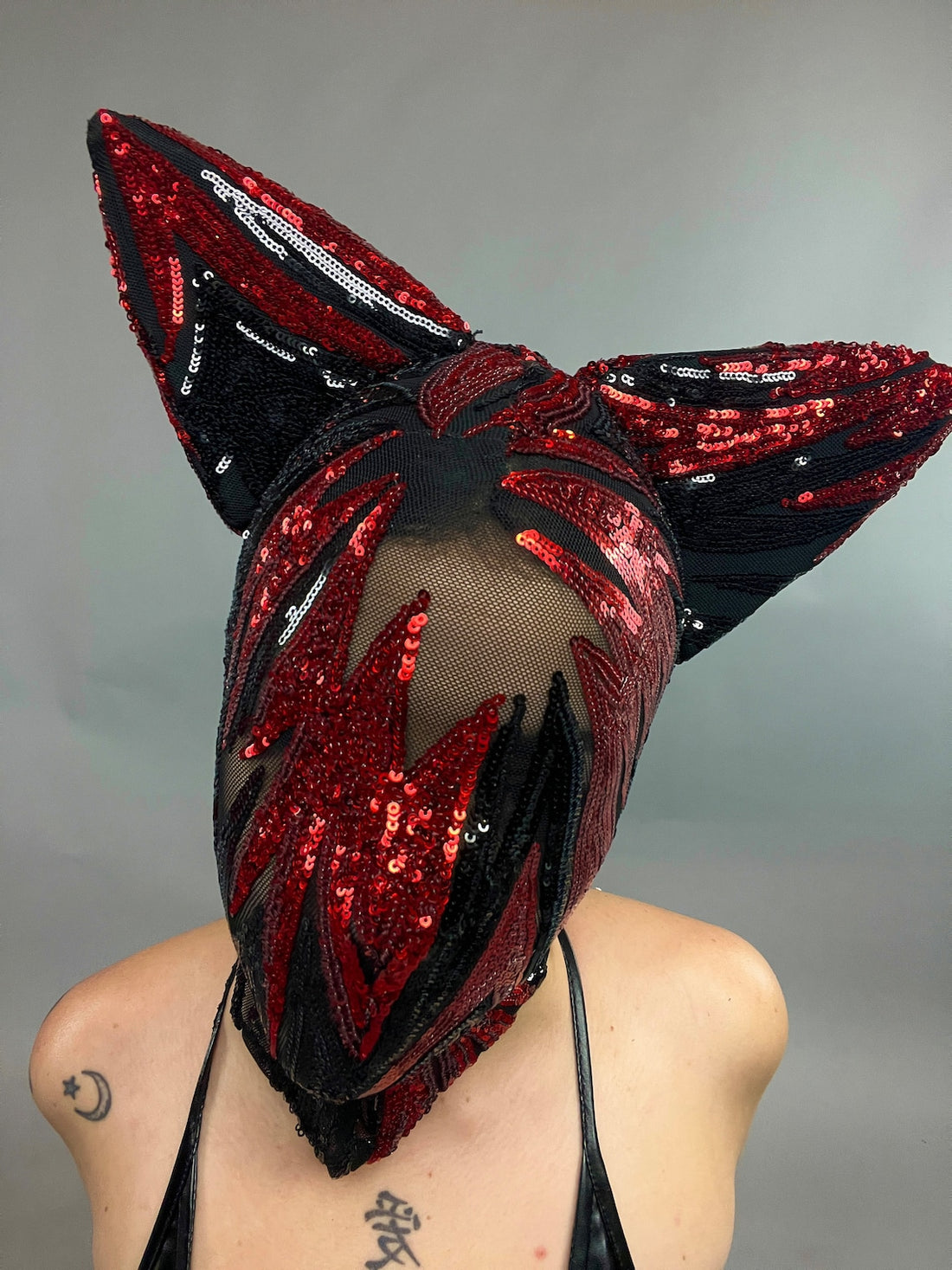 In a studio, a person wears the Cat Ears Sequin Headpiece—a red and black sequined mask with large cat ears—creating a futuristic clothing look.