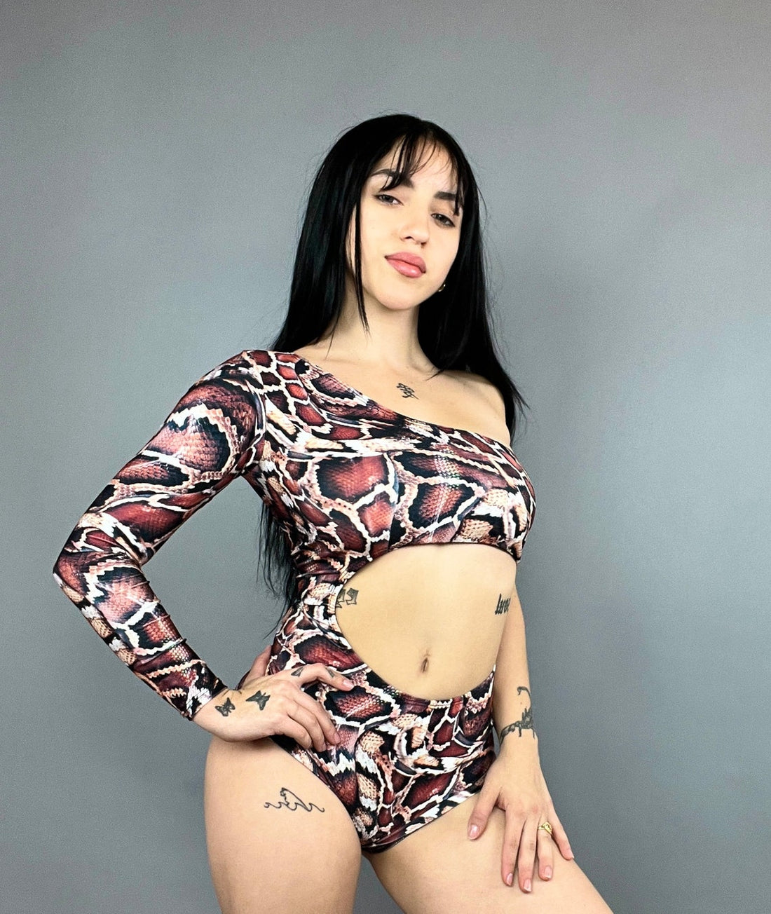 A person stands confidently against a plain background in a snake-print, one-sleeve Leotard Costume for Gymnasts, Circus Outfit, Futuristic Clothing, Exotic Dance Wear, or Pole Dance Costume.