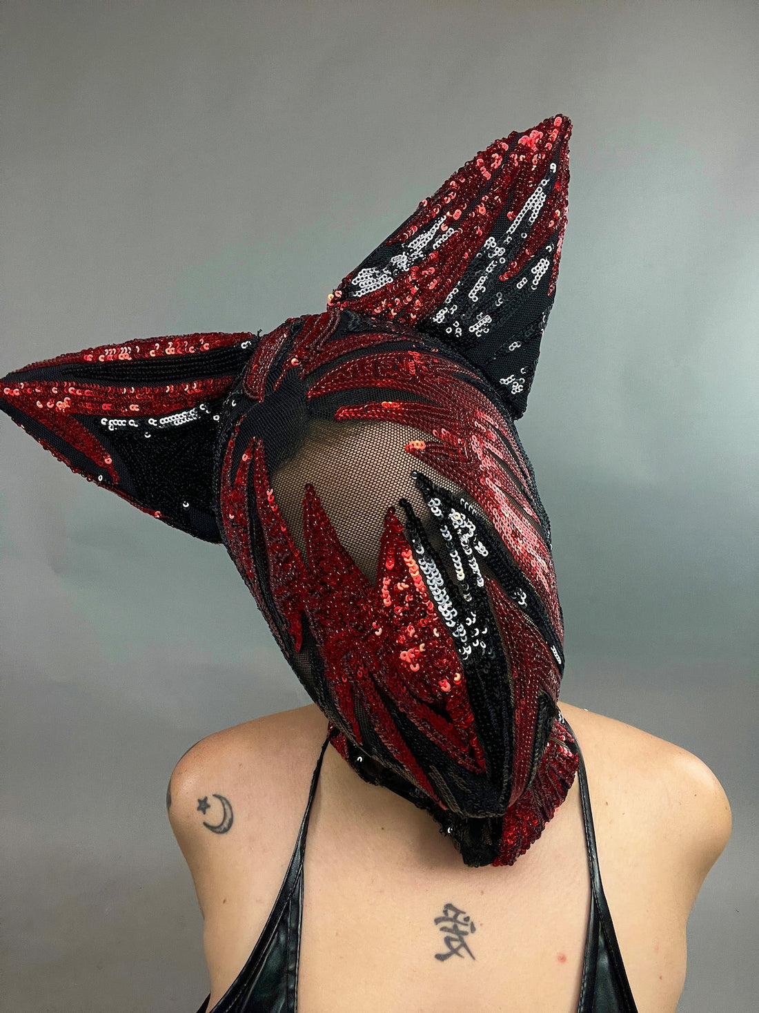 A person sports the Cat Ears Sequin Headpiece and Beautiful Sequin Face Mask, showcasing red and black patterns with cat-like ears, creating a futuristic and edgy ensemble.