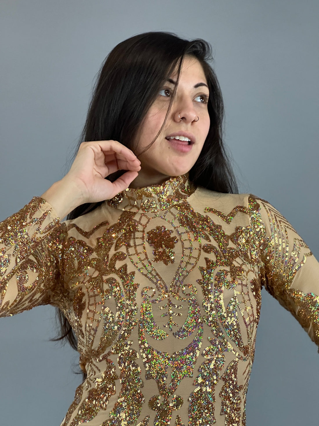 A woman in a glittery Gold Sequin Catsuit with full sleeves poses against a gray background, showcasing its versatile design as part of the Gold Fairy Costume.