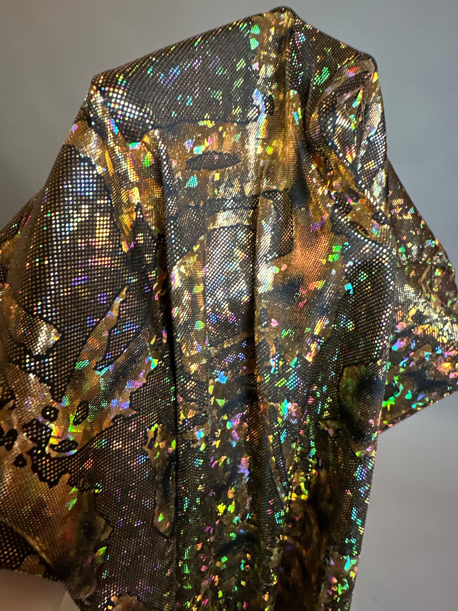 A vibrant, iridescent fabric adorned with a multicolored starry design elegantly wrapped over a form against a simple backdrop, evocative of the Alien Costume lycra jumpsuit.