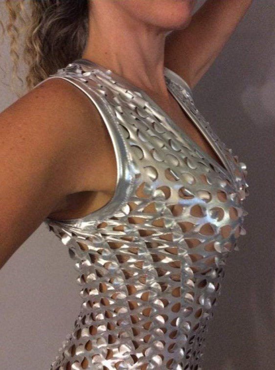 In a side view, a person showcases the Silver Sleeveless Catsuit with interlinked rings and a spiky texture, embodying futuristic fashion with their raised arm.