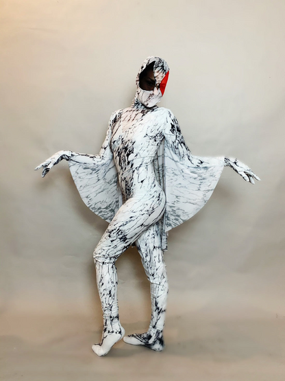 A person in a black and white full body catsuit, with wings, face mask, gloves, and socks featuring a marble pattern and red face detail, elegantly poses against a plain backdrop.