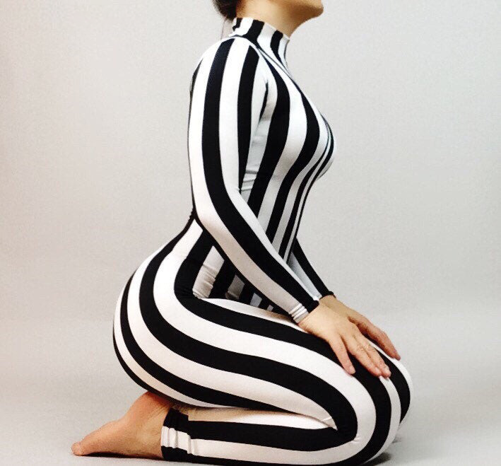 A person kneels side-on in a sleek Black and White Stripes Catsuit, Full Sleeves, Turtleneck—ideal for festivals. The custom sizing ensures a flawless fit against the plain background.