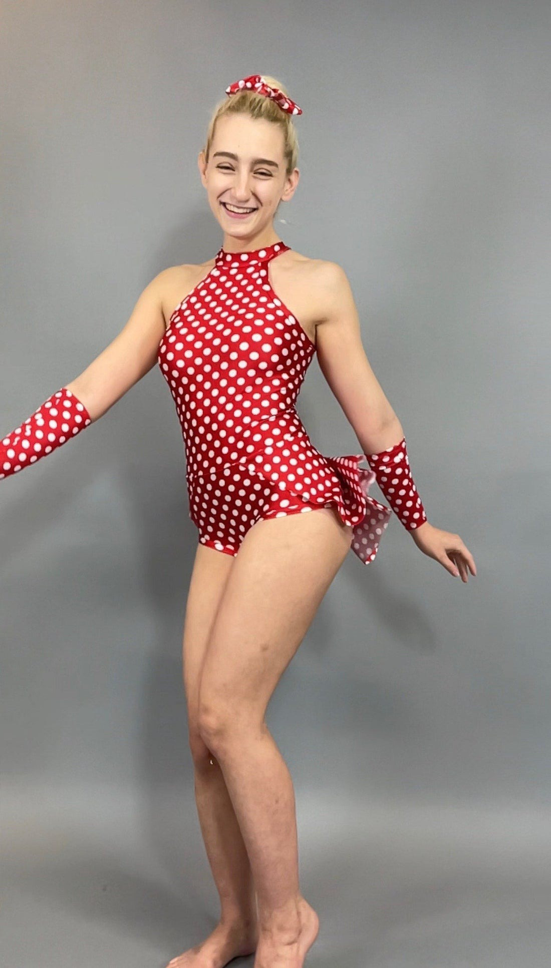 A person in a red polka dot outfit poses enthusiastically against a gray background, reminiscent of the Exotic Dance Wear Burlesque Bodysuit with Skirt, perfect for showgirls and pole dancers.