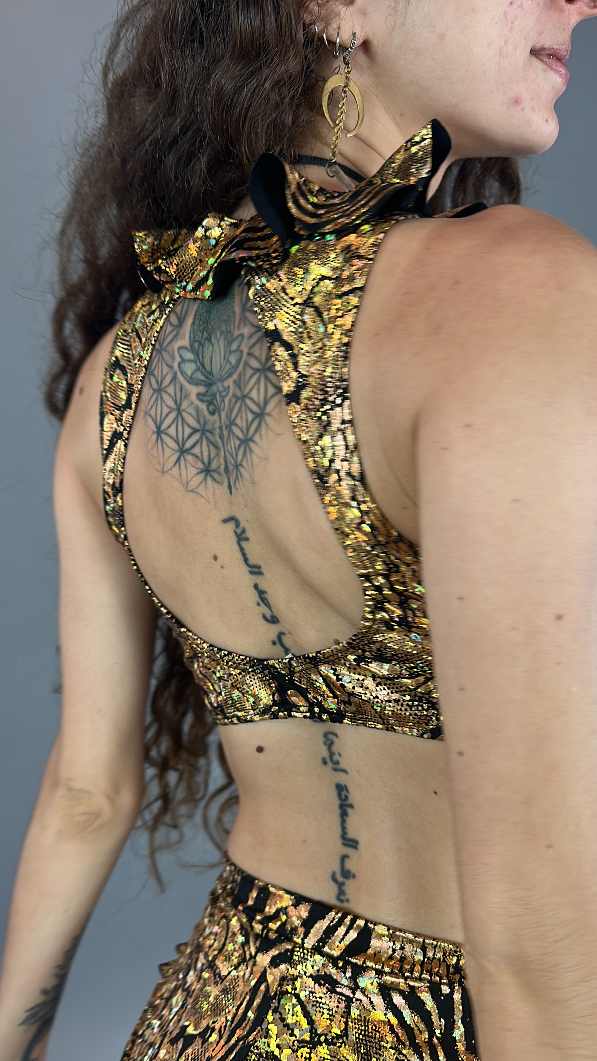 A tattooed individual sparkles in a Gold &amp; Black Snakeskin crop top and bottom set with floral earrings, exuding the flair of a pole artist&