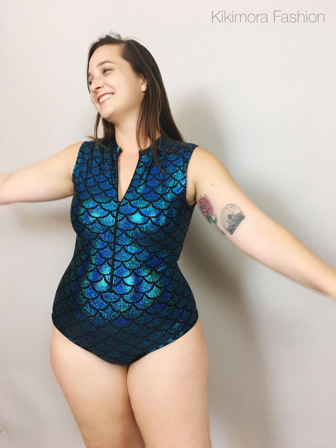 A person in a custom-made turquoise and black pattern leotard smiles with arms outstretched against a plain background, highlighting the elegance of the 4-way stretch lycra.