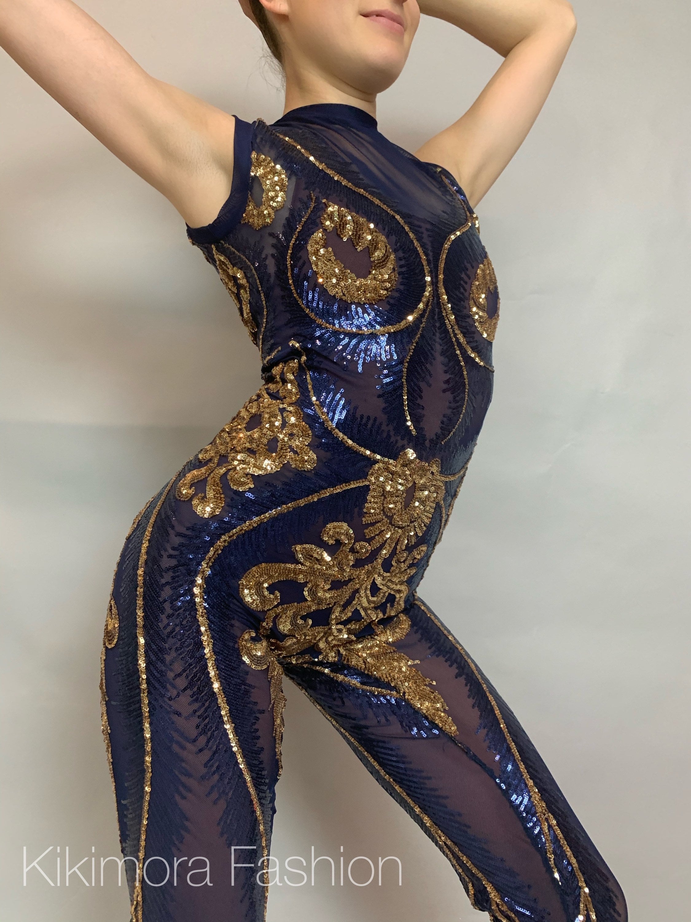 Person posing in a sleeveless, mock turtleneck Blue And Gold Sequin Catsuit, hands behind their head, evoking a gymnastic flair.