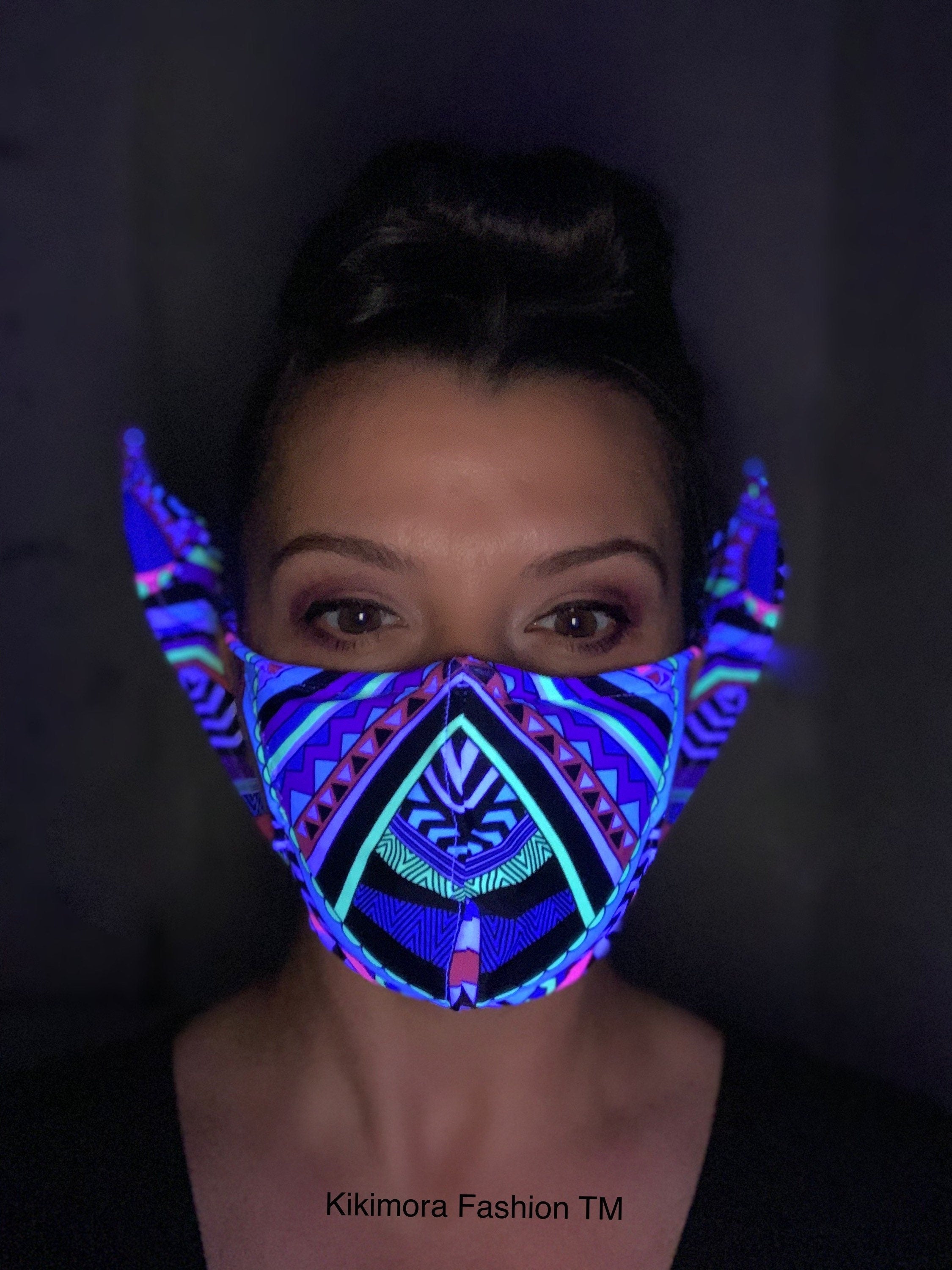 Person wearing a Glow Face Mask With 5 Layer HEPA Filter, a striking fashion accessory featuring tribal-inspired patterns that glow vividly under blacklight, highlighting unique Kikimora Fashion style.