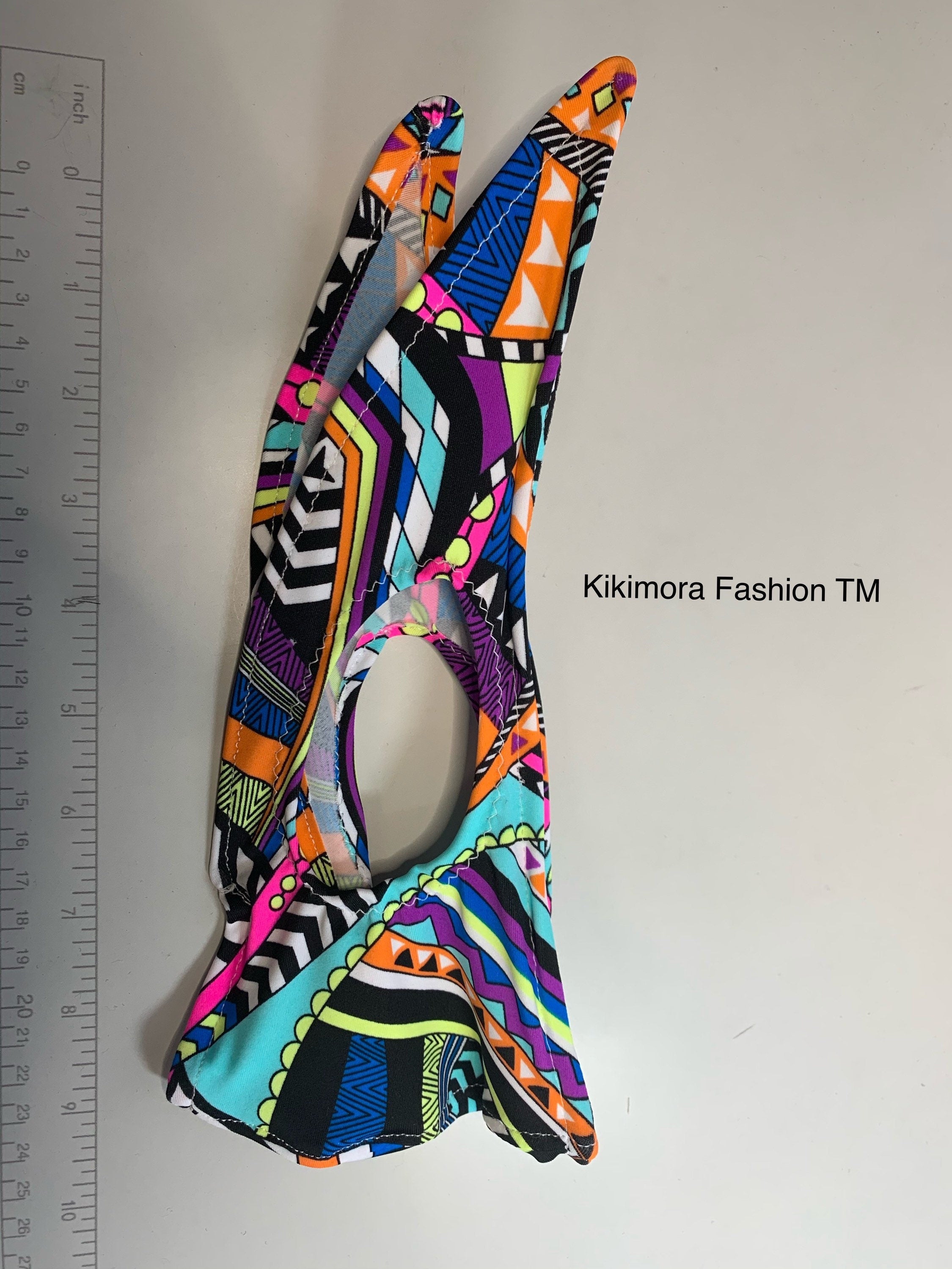 Glow Face Mask With 5 Layer HEPA Filter, Fashion Accessory—featuring vibrant geometric patterns beside a ruler; text reads "Kikimora Fashion TM." A standout in sustainable fashion.